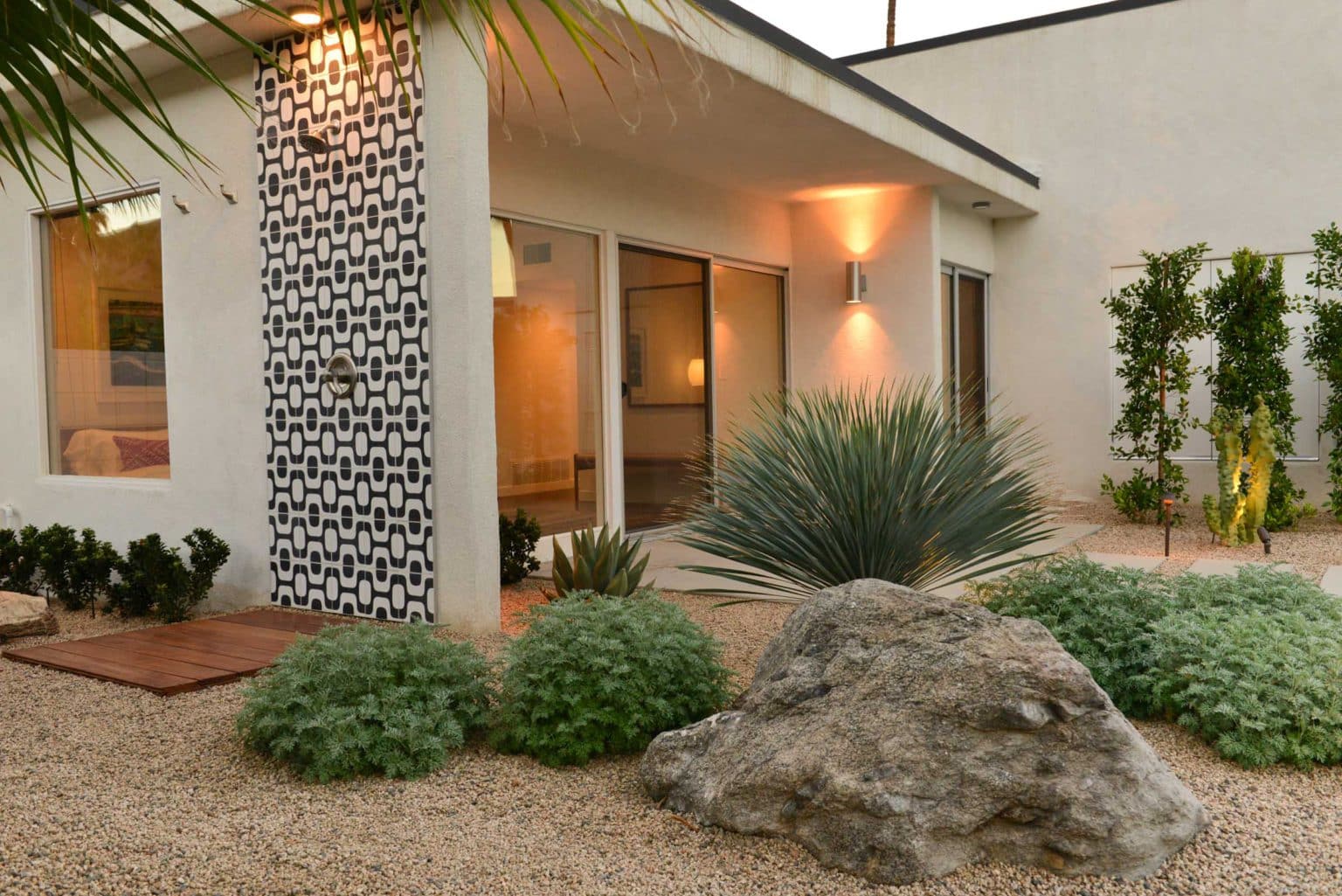 Complete residential landscape design and installation in Palm Springs, including hardscape, custom outdoor shower with tile, fire feature, low voltage lighting, boulders, artificial turf, irrigation and desert plants.