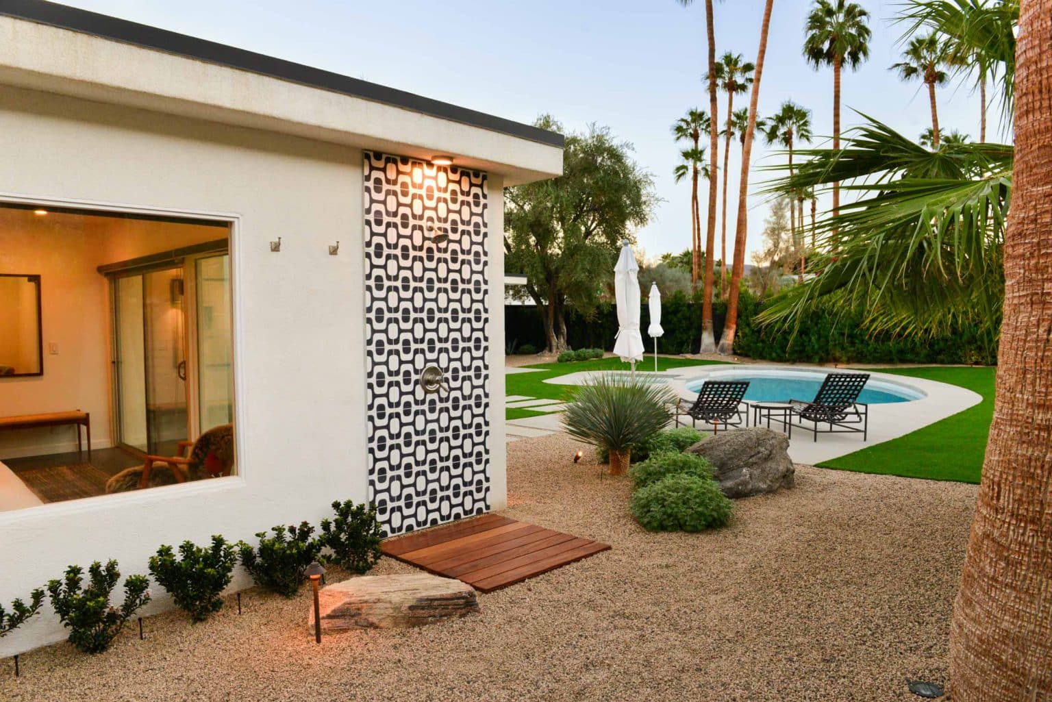 Complete residential landscape design and installation in Palm Springs, including hardscape, custom outdoor shower with tile, fire feature, low voltage lighting, boulders, artificial turf, irrigation and desert plants.