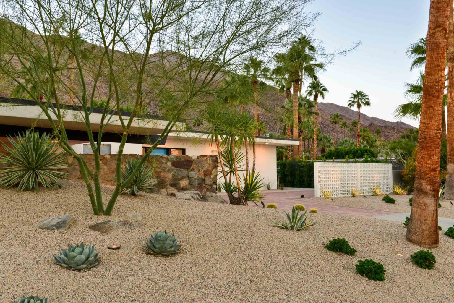 Complete residential landscape design and installation in Palm Springs, including hardscape, custom outdoor shower with tile, fire feature, low voltage lighting, boulders, artificial turf, irrigation and desert plants.