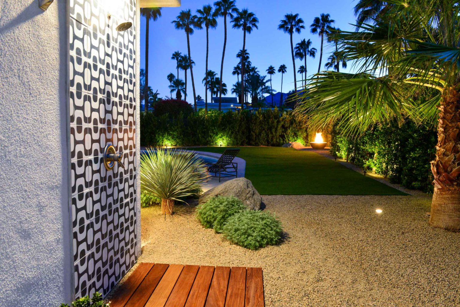 Complete residential landscape design and installation in Palm Springs, including hardscape, custom outdoor shower with tile, fire feature, low voltage lighting, boulders, artificial turf, irrigation and desert plants.