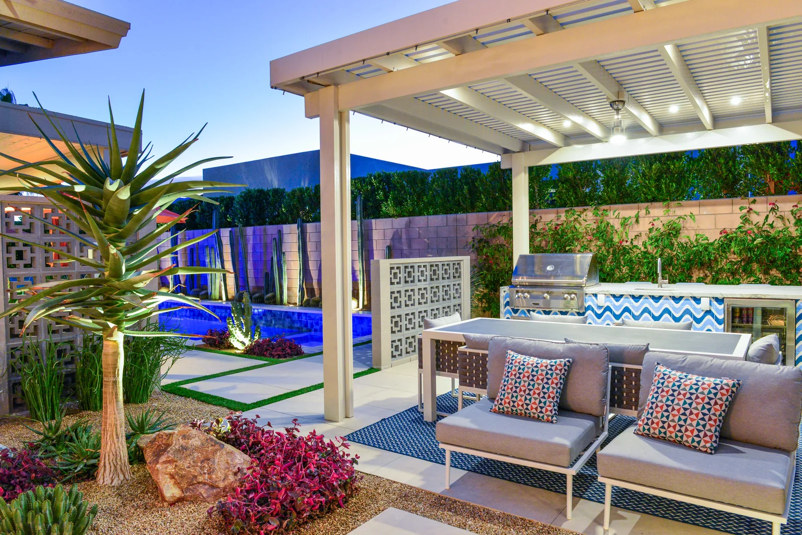Bliss Way after dark: lit shade structure over the BBQ island and lounge, breeze block screen and planting