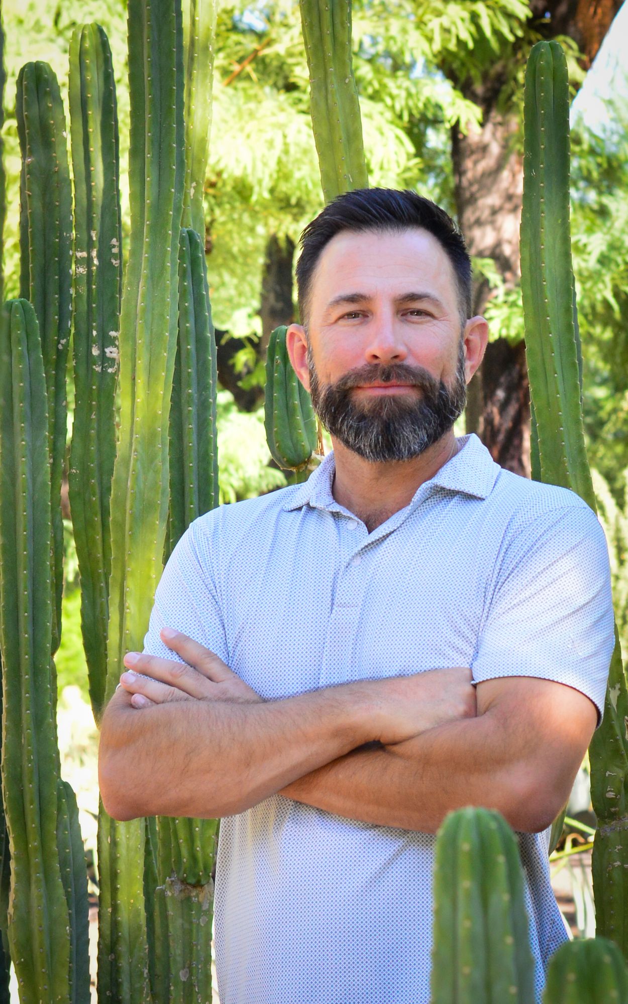 Gus Diaz — Founder & Landscape Contractor Gus Diaz, founder of Gus Landscape Contractors, standing with arms crossed among tall columnar cacti